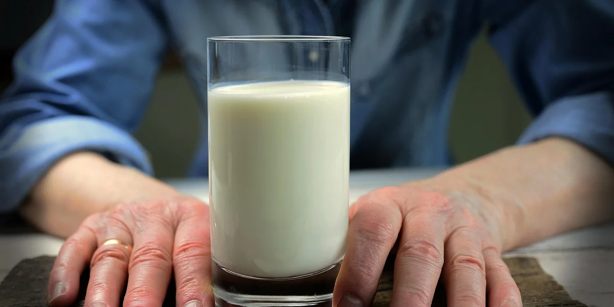 Close-up of a glass of milk held by hands resting on a table, symbolizing calcium intake.