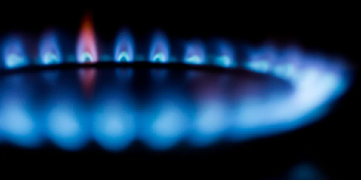 Close-up of a blue gas burner flame with a red tip against a dark background.