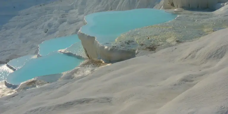 Turquoise mineral pools with white travertine terraces in a natural landscape.
