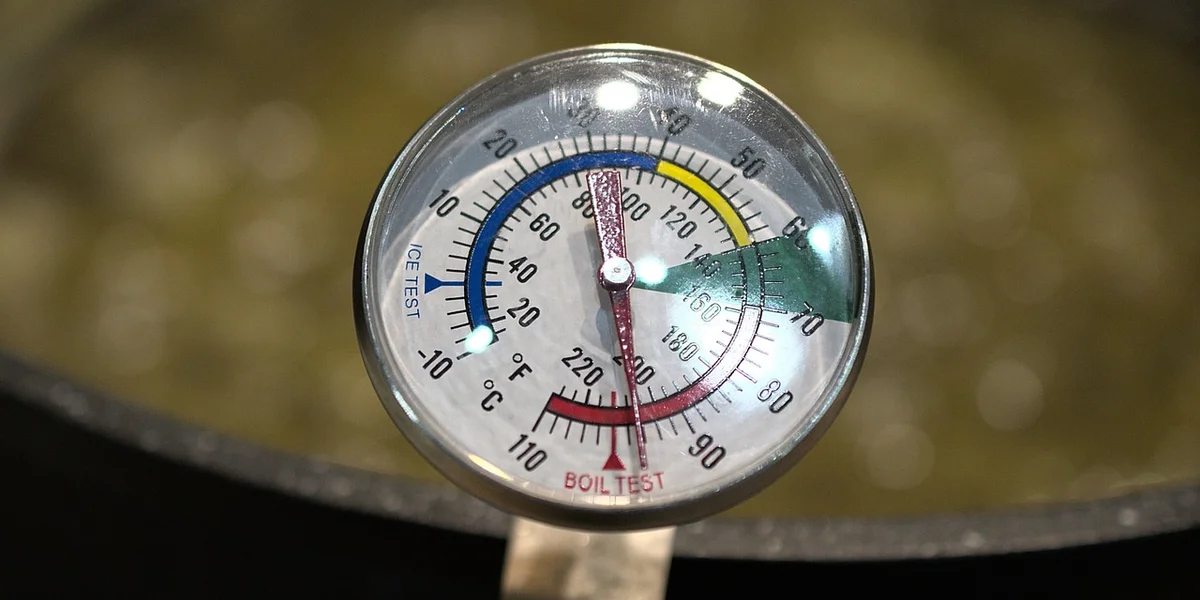 Close-up of a round analog thermometer with color-coded temperature zones, used to monitor a gecko enclosure's heat gradient.