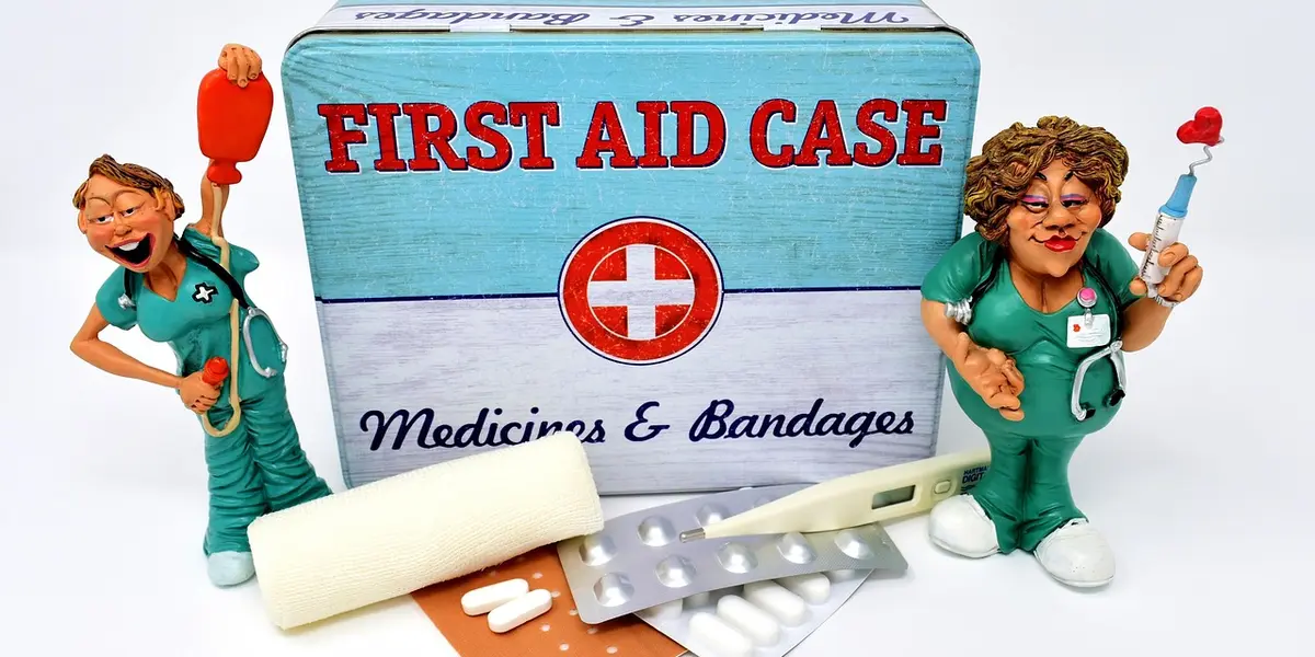 Two cartoon nurses stand beside a blue first aid case labeled 'First Aid Case', with medicine and bandages laid out in front.