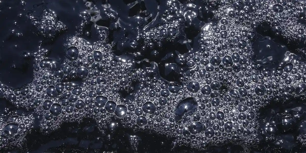 Close-up of dark bubbles on a liquid surface, evoking the bubbly foam texture used for crafting a gecko terrarium background.
