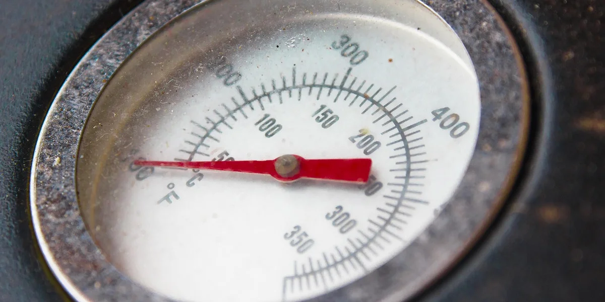 Close-up of a circular dial thermometer with a red needle.