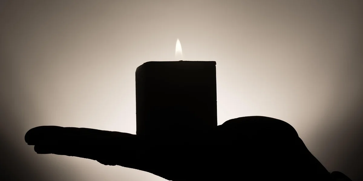 Silhouette of a hand holding a lit candle against a soft, dark background