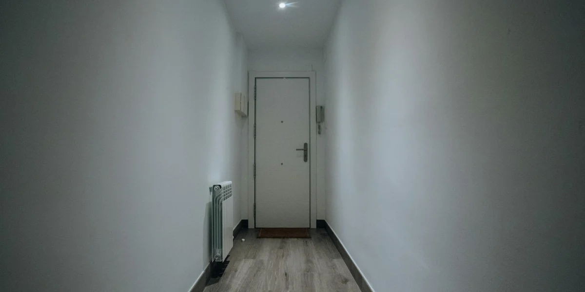 Narrow hallway with a door at the end and a radiator along the left wall.