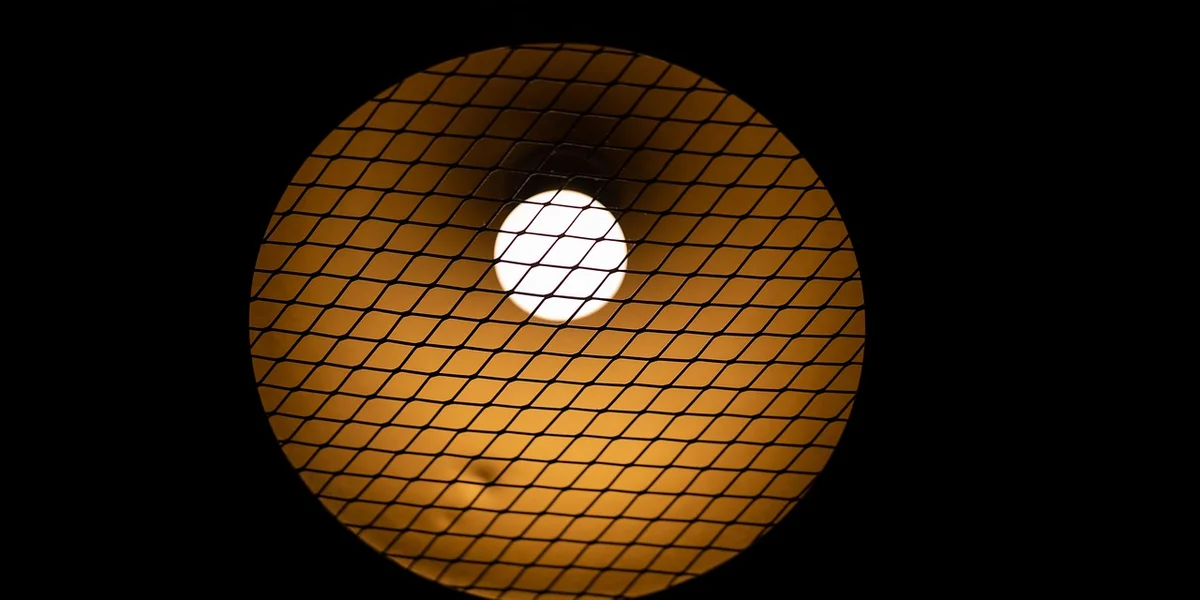 Close-up of a UVB bulb inside a lamp with a protective mesh grid, illustrating gecko enclosure lighting.