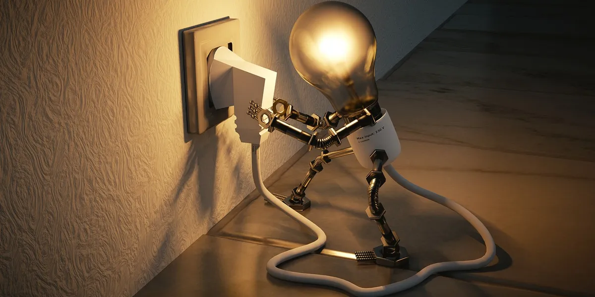 A lamp with a light bulb stands on the floor near a wall outlet, with tangled cords extending across the room.