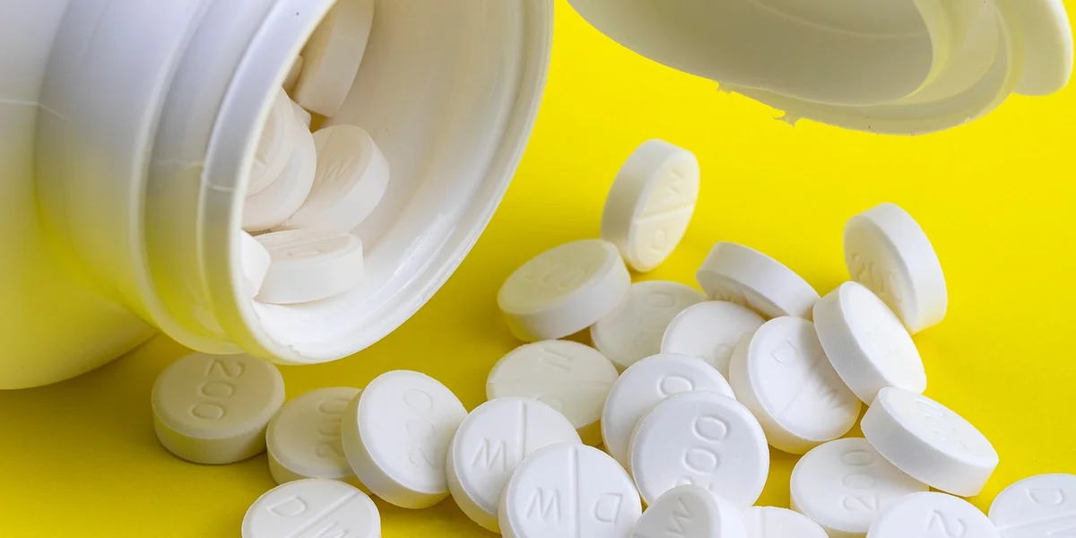 White vitamin tablets spilled from a white bottle onto a bright yellow background, illustrating supplements used in reptile care.