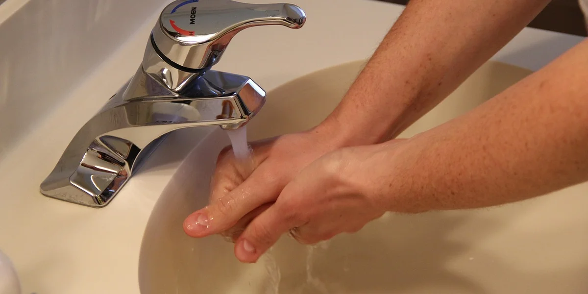 Hands being washed under running water at a sink to promote hygiene before handling geckos