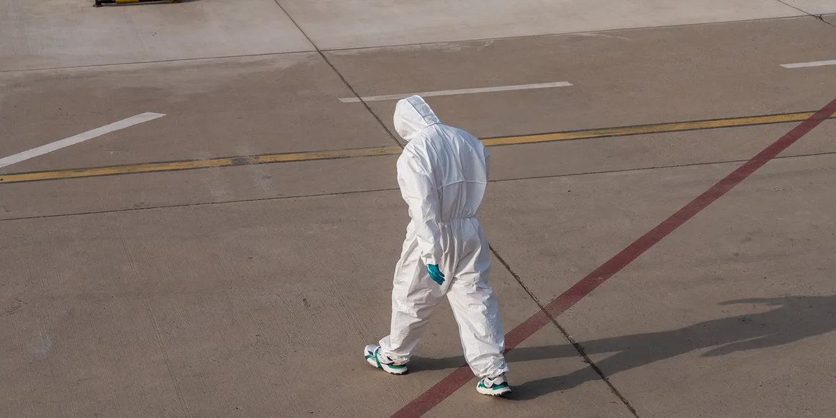 Person wearing a white hazmat suit walking on a concrete tarmac, illustrating biosecurity during quarantine.