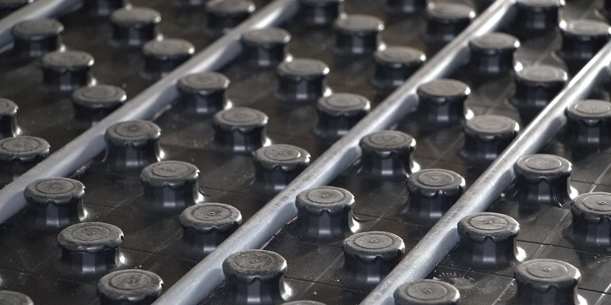 Close-up of a black heating mat with a grid of circular nodes and metal rails, illustrating typical installation surface.