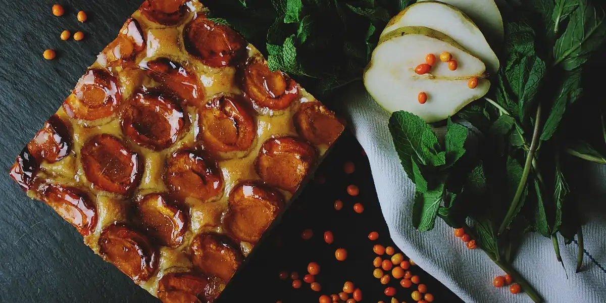 Pizza with pepperoni slices on a dark surface, accompanied by leafy greens and white fruit slices with small orange beads.