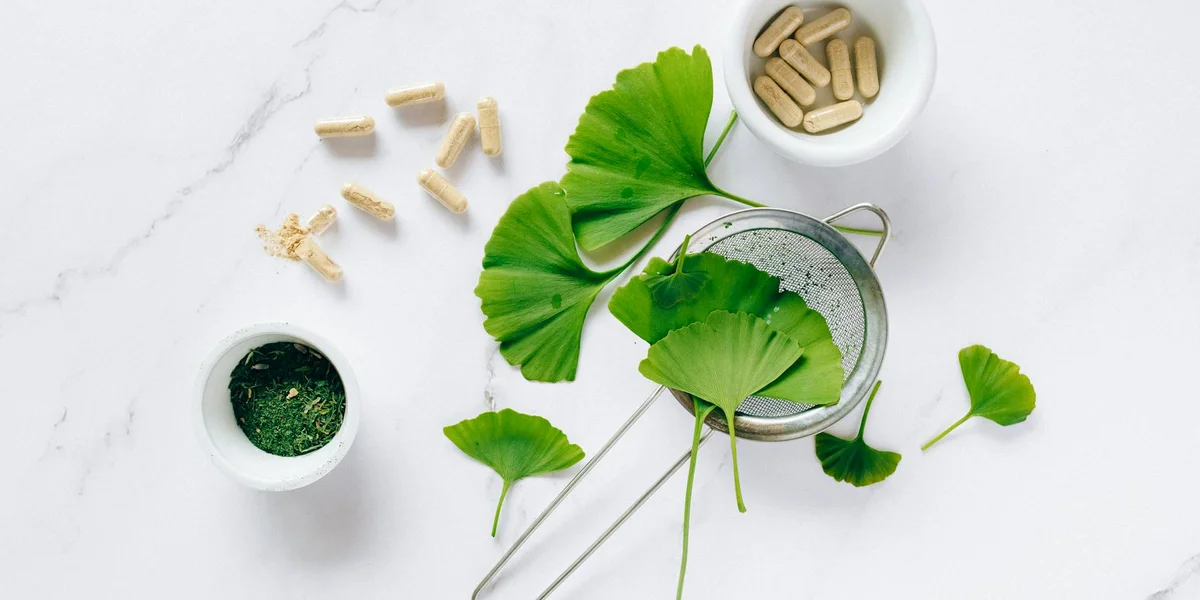 Assorted supplements and leafy greens arranged on a white surface to illustrate calcium and vitamin D3 management for leopard geckos