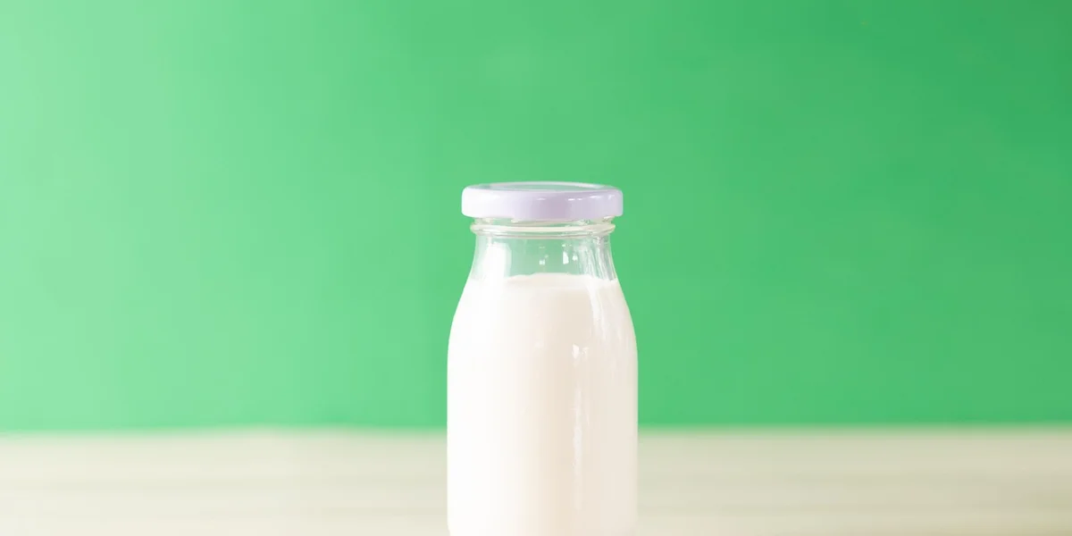 Bottle of milk on a light surface with a green background, symbolizing calcium intake for bone healing and rehabilitation.