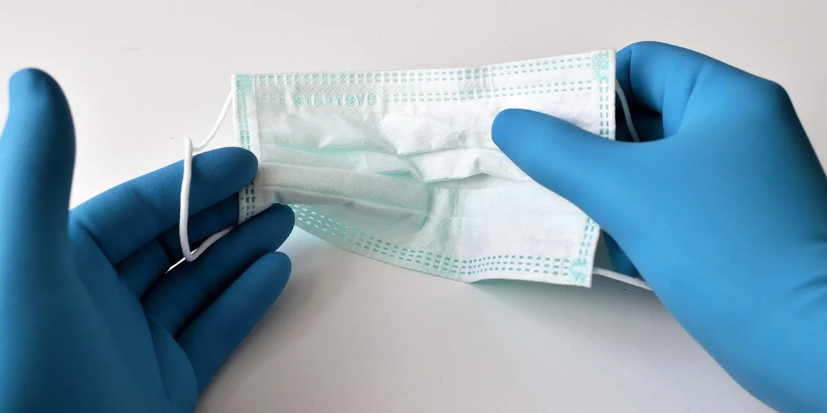 Blue disposable gloves hold a surgical mask, illustrating PPE use during quarantine.