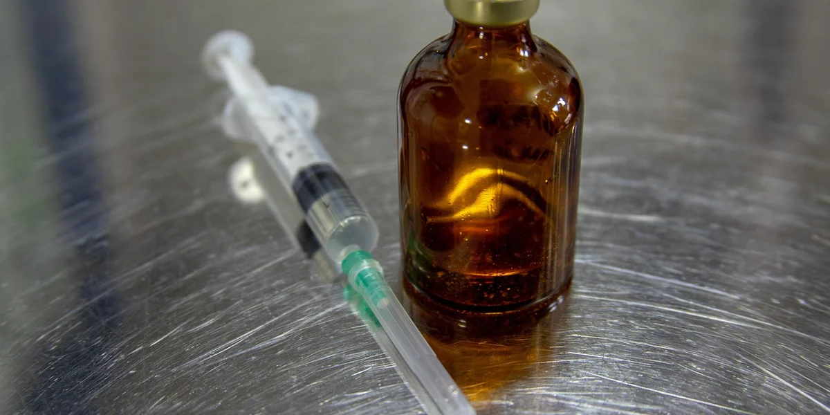 Syringe and amber medicine bottle on a stainless steel surface, representing veterinary care for reptiles