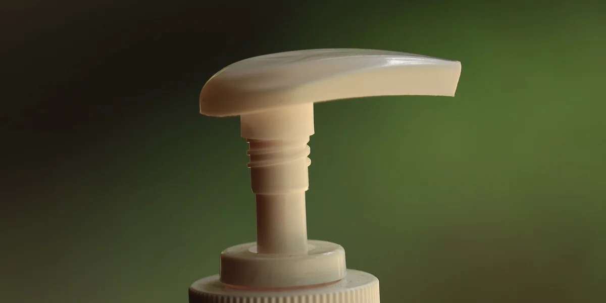 Close-up of a soap dispenser pump with a soft green background, emphasizing handwashing.