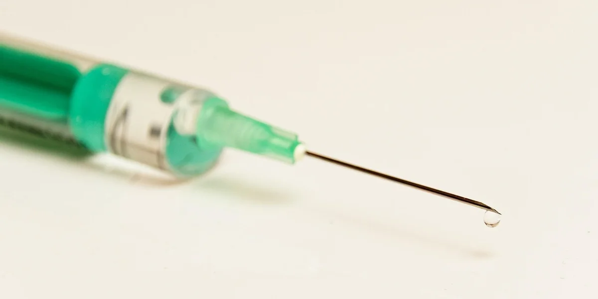 Close-up of a syringe with a green-tinted plunger on a white surface
