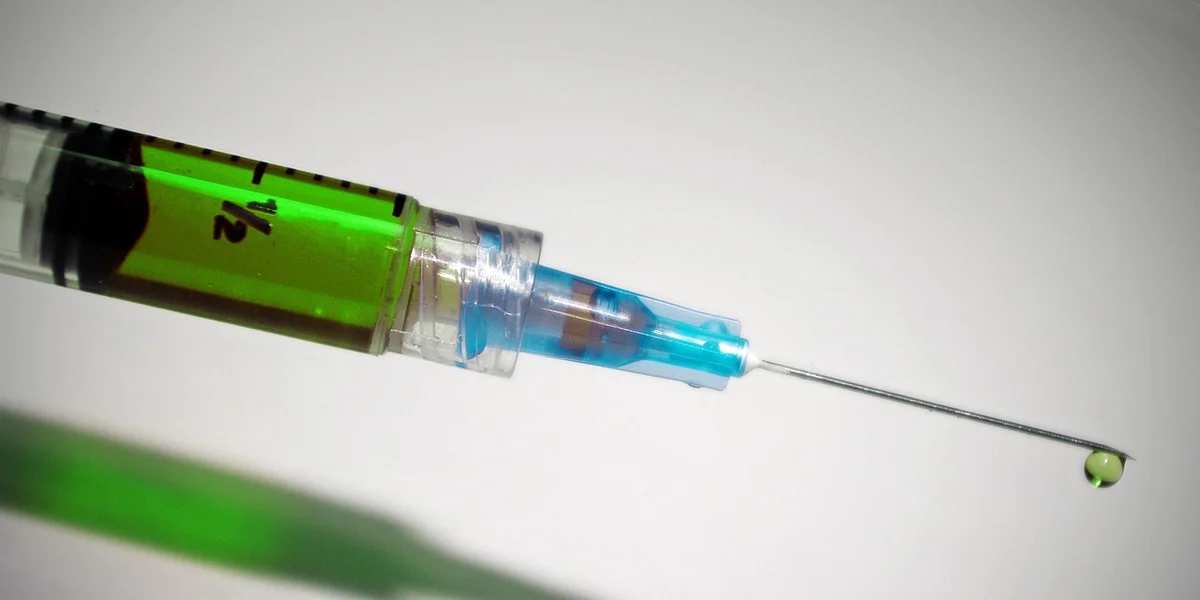 Close-up of a syringe with green liquid and a single drop at the needle tip.