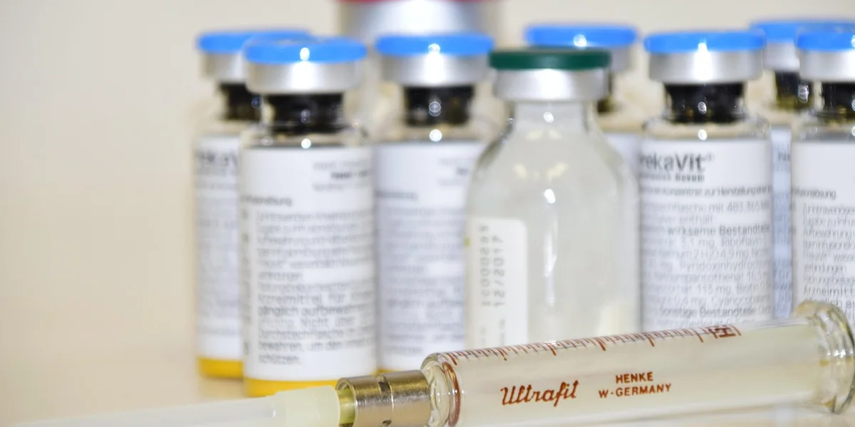 Row of medicine vials with blue caps and a syringe in the foreground on a light counter.